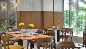 Un comedor con mesas y sillas de madera, algunas con cojines. Hay jarrones con flores amarillas sobre las mesas.