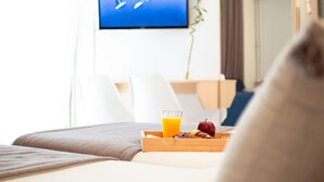 Habitación de hotel con cama, bandeja de desayuno con jugo de naranja y un televisor mostrando un velero.