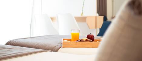 A hotel room with a bed, a breakfast tray with orange juice, and a TV displaying a sailboat.