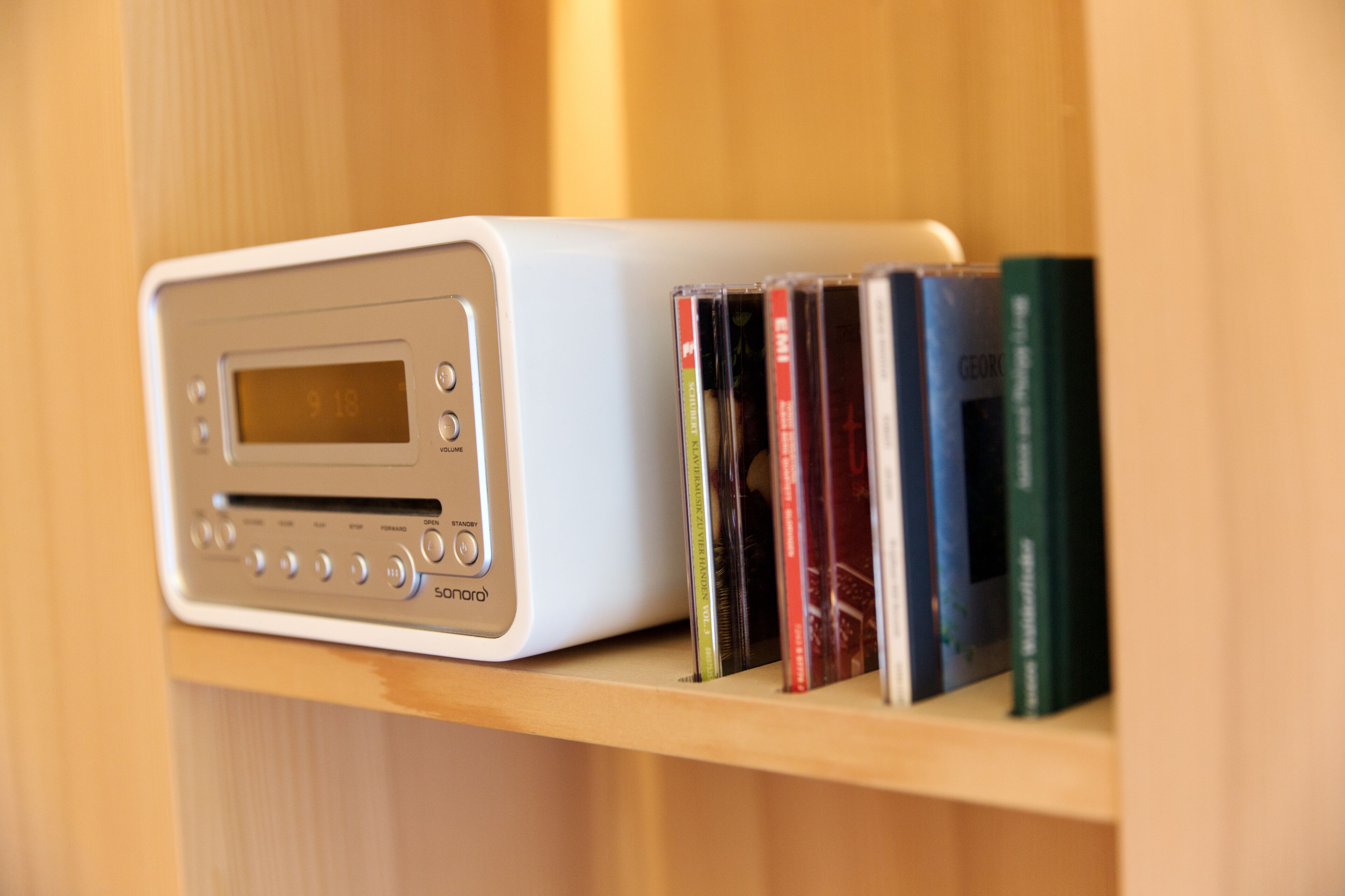 Ein weißes, tragbares Sonora-Radio auf einem Holzregal mit einer Reihe von Büchern.