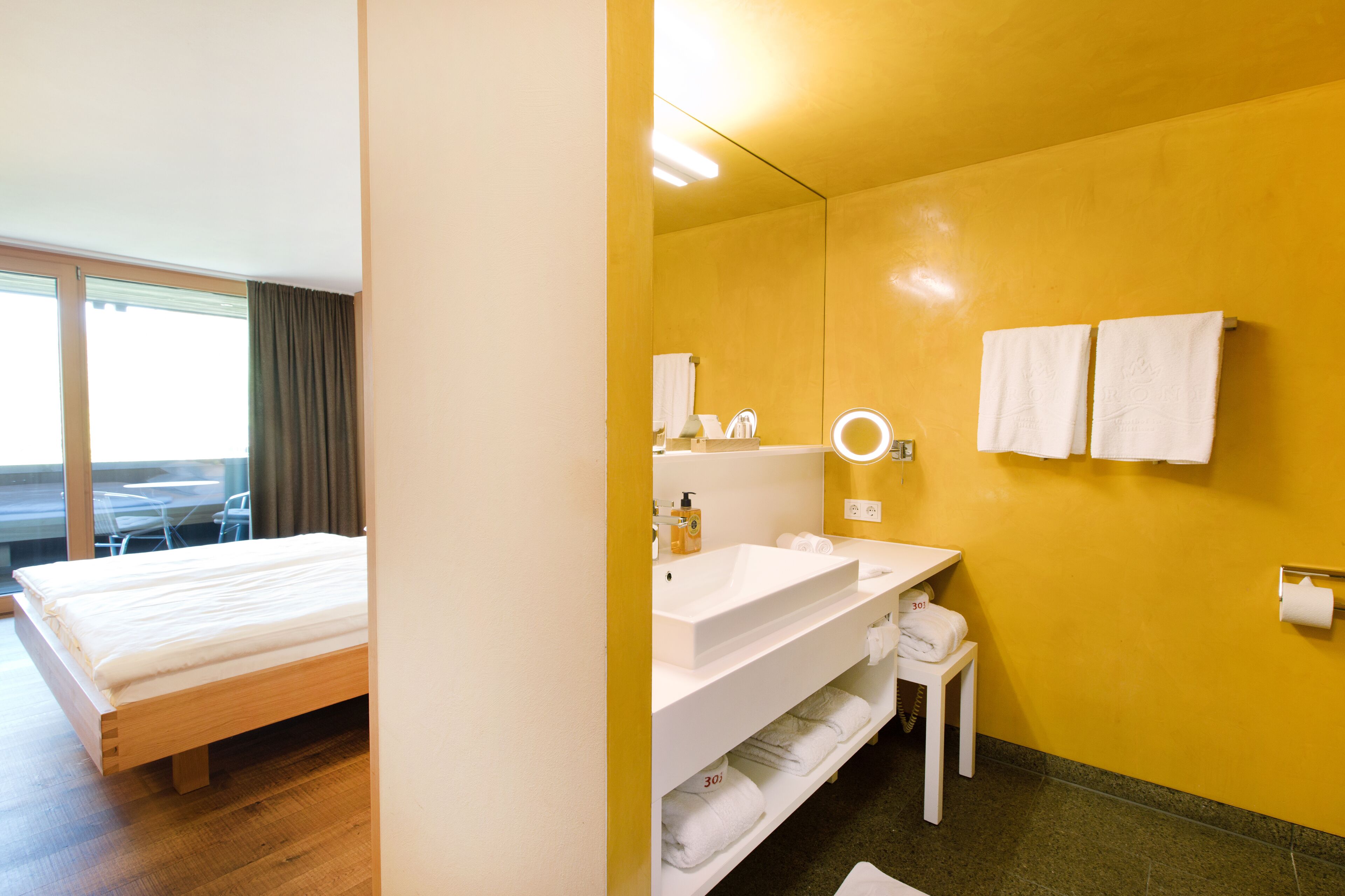 A hotel room with a bed, a bathroom with a sink, mirror, and towels.