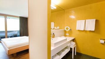 A hotel room with a bed, a bathroom with a sink, mirror, and towels.