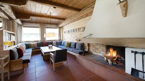 A cozy living room with a fireplace, wooden beams, a sofa, and a dining table. -  Krone Hittisau - Hotel & Restaurant im Bregenzerwald (Hittisau)