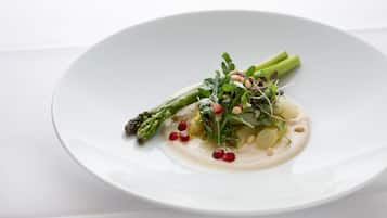 Un plato blanco con un guiso de comida que incluye espárragos, verduras de hoja verde y semillas de granada.