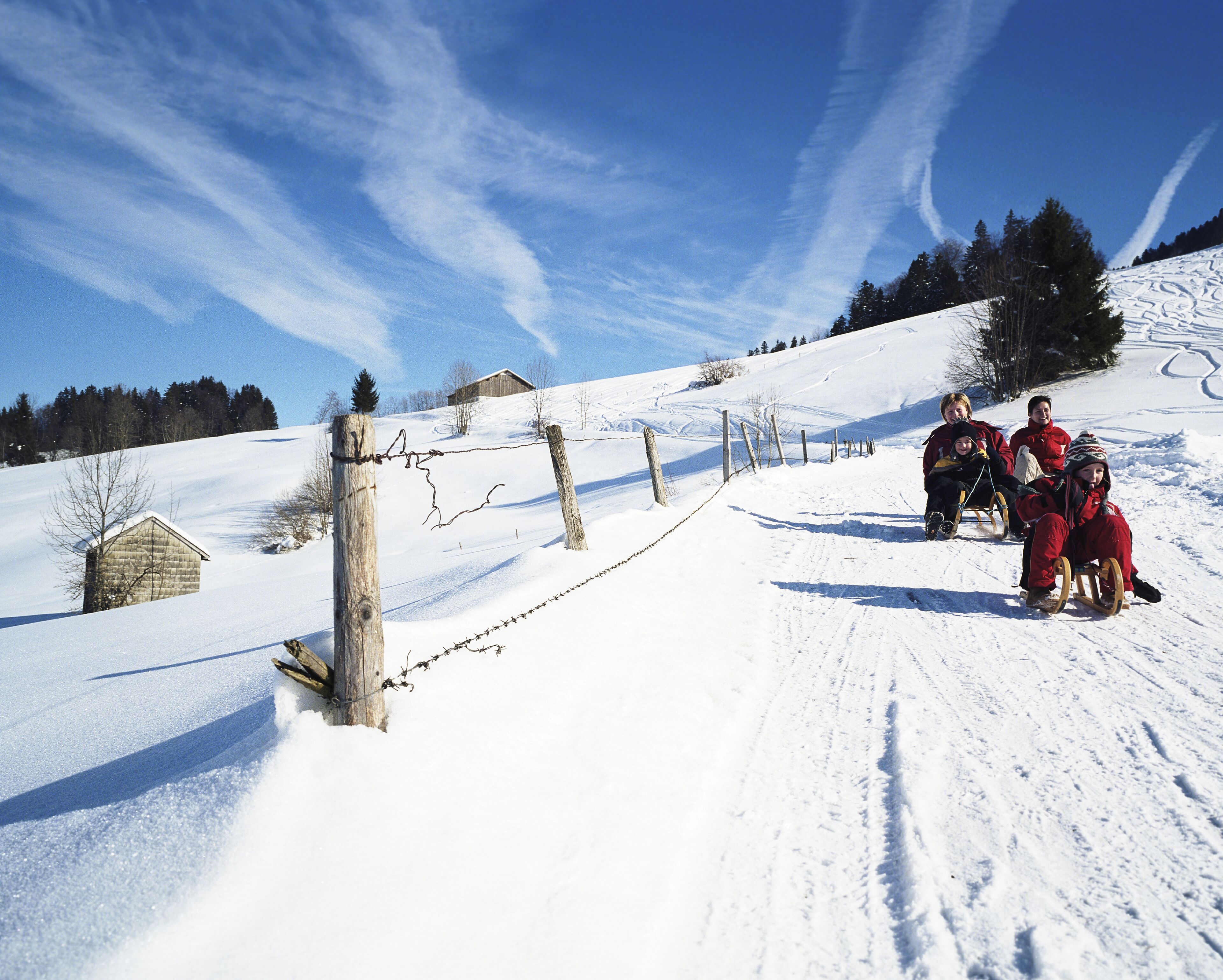 A snowy landscape with a wooden fence, a small wooden structure, and a clear blue sky.