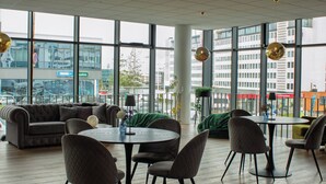 A modern interior with a round table and chairs, a sofa, and large windows offering a city view. - Hótel Múli (Reykjavik)