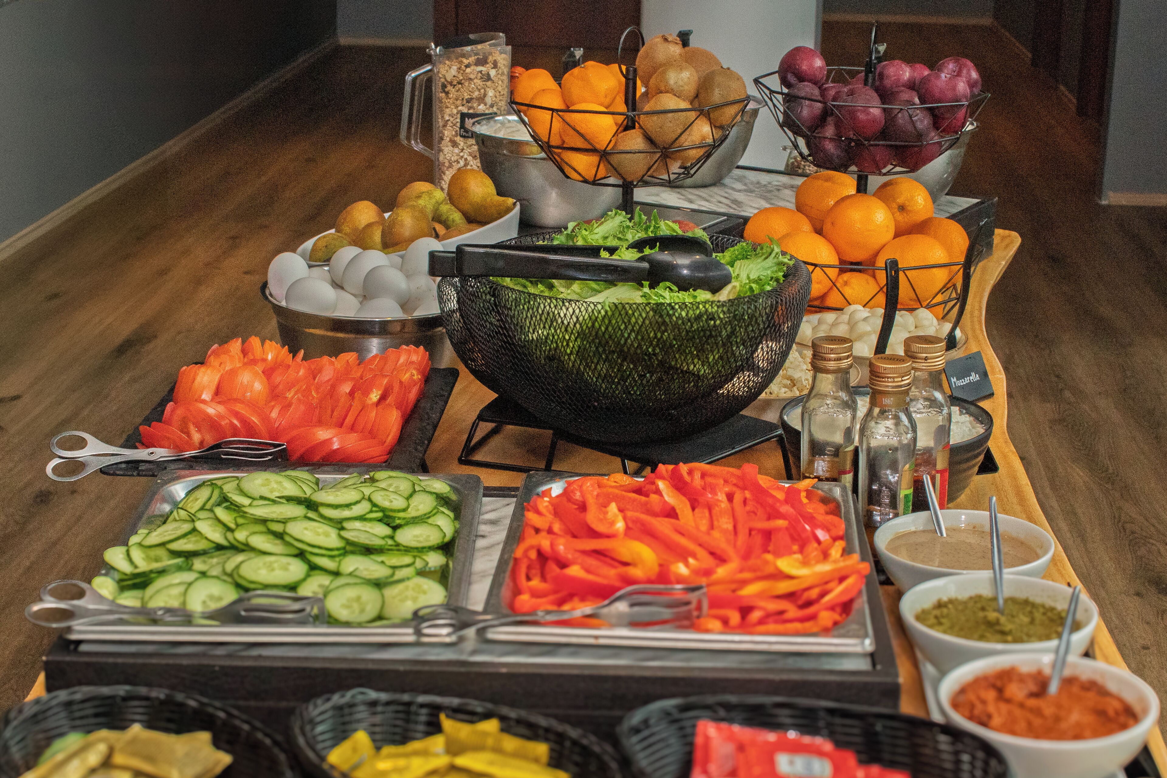 A buffet table with various food items including fruits, vegetables, and condiments.