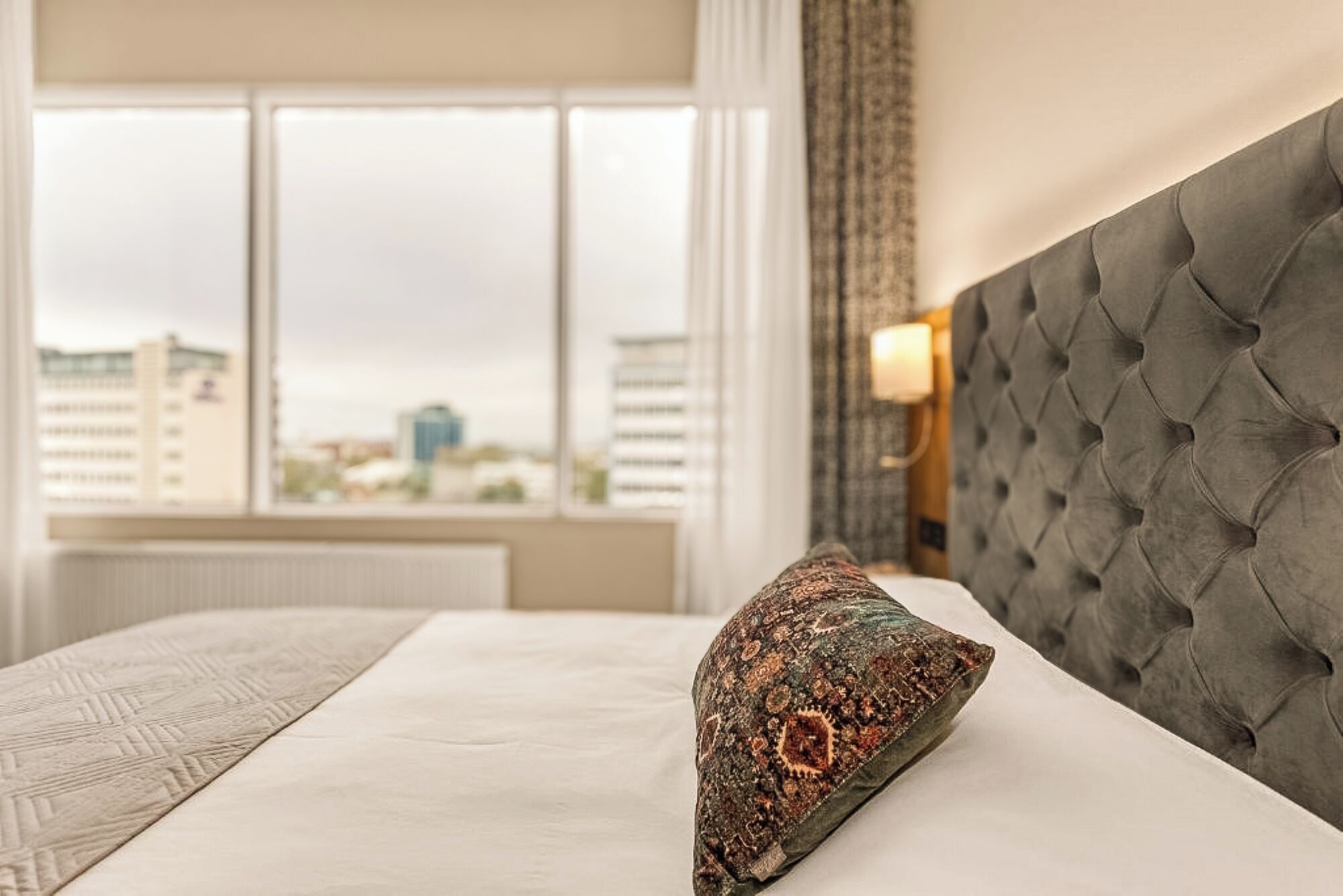 Une chambre d’hôtel dotée d’une grande fenêtre, d’une tête de lit capitonnée et d’un coussin à motifs.