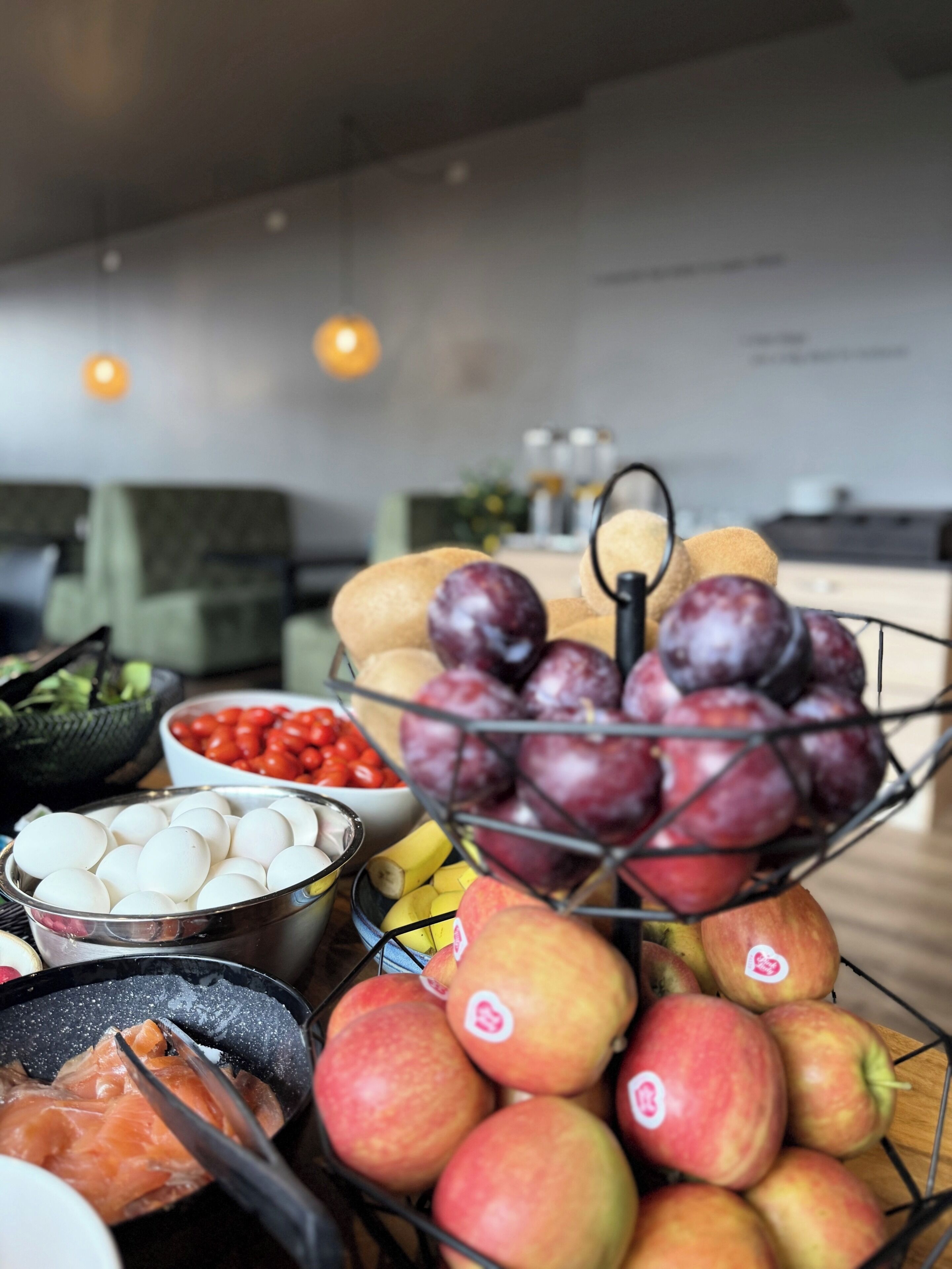 A fruit and egg display with a bowl of tomatoes and a basket of plums.