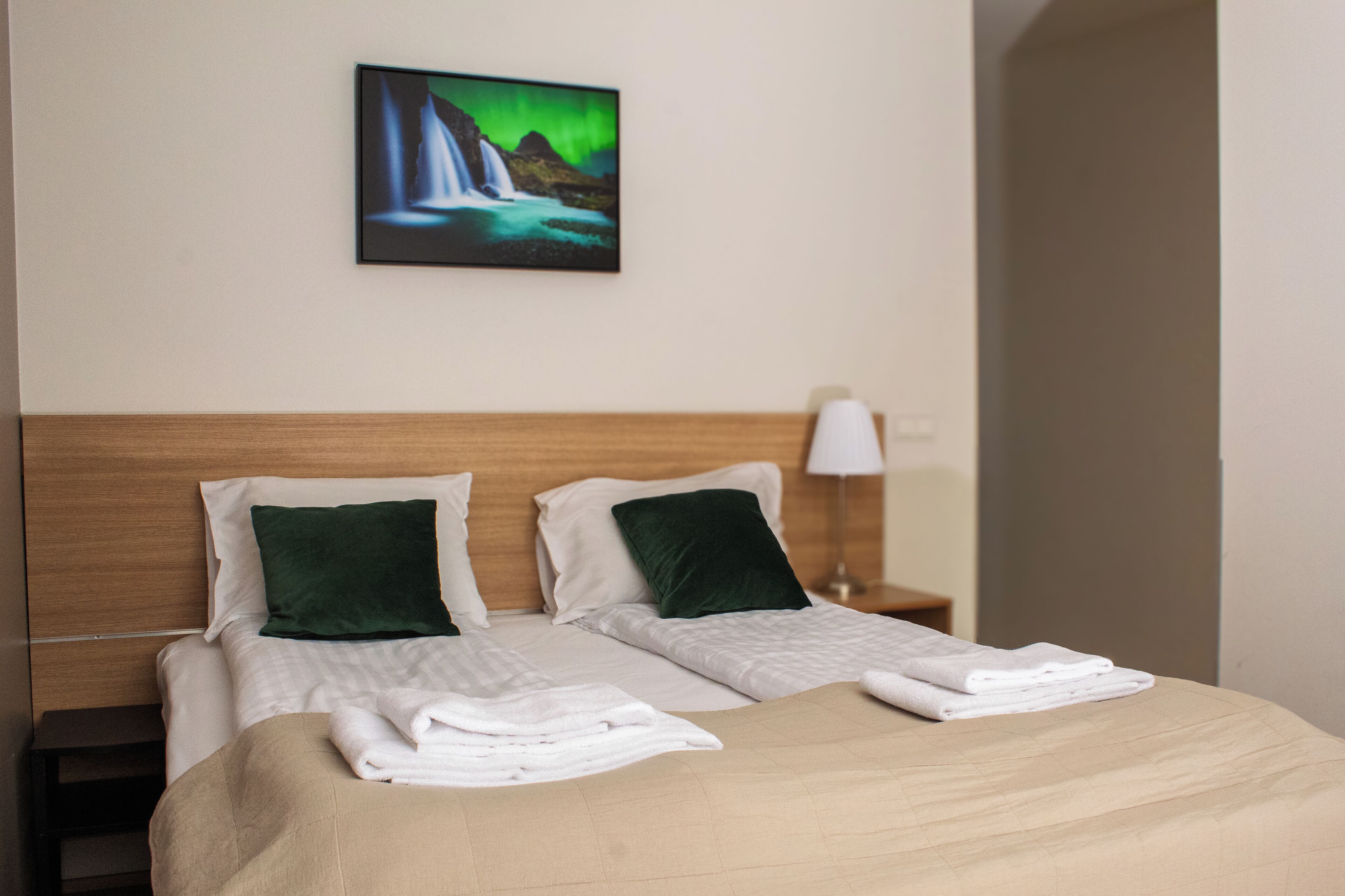 A hotel room with a bed, two pillows, a nightstand with a lamp, and a painting of a waterfall.