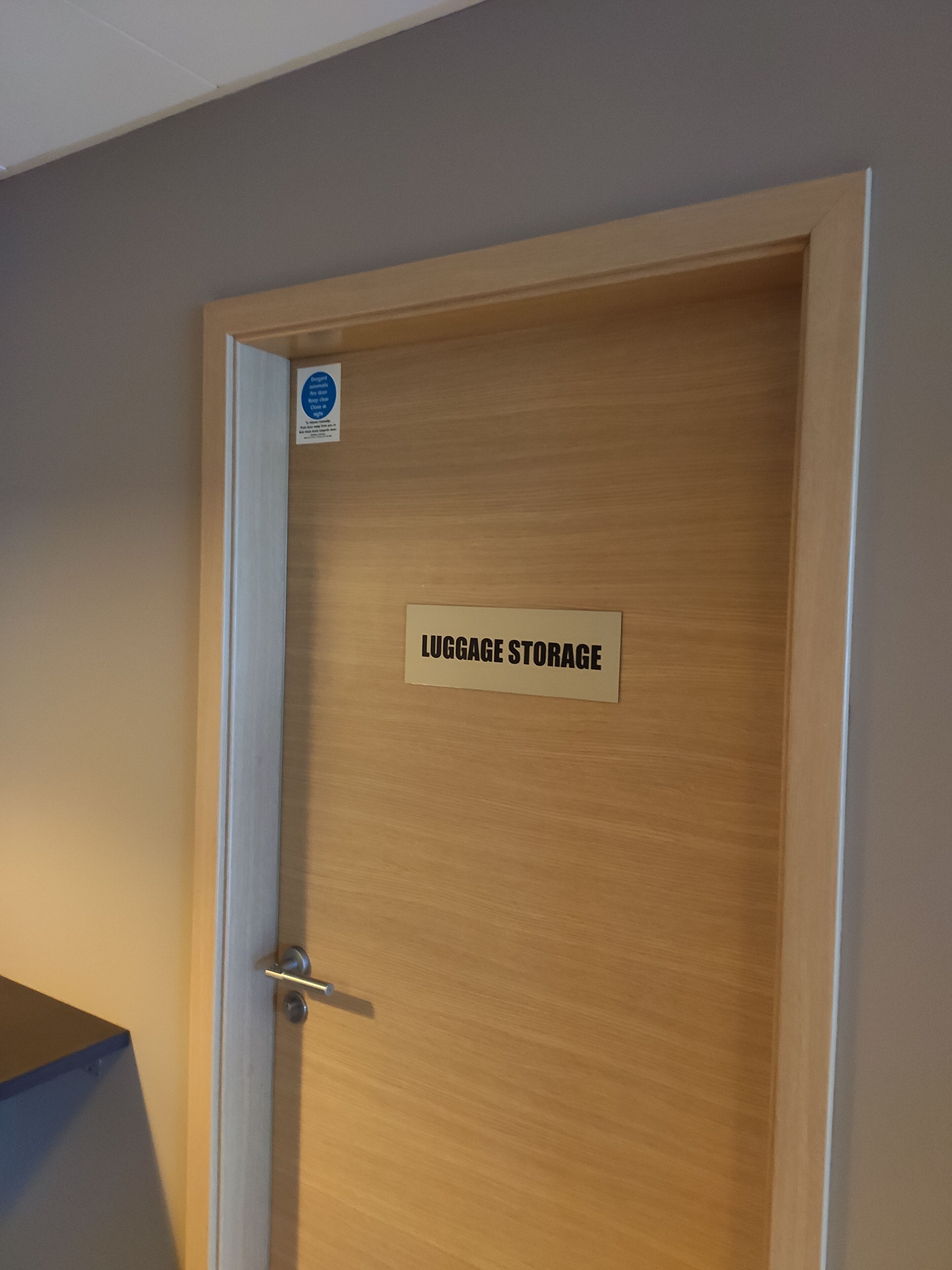 Una puerta de madera con un cartel que dice 'LUGGAGE STORAGE'.