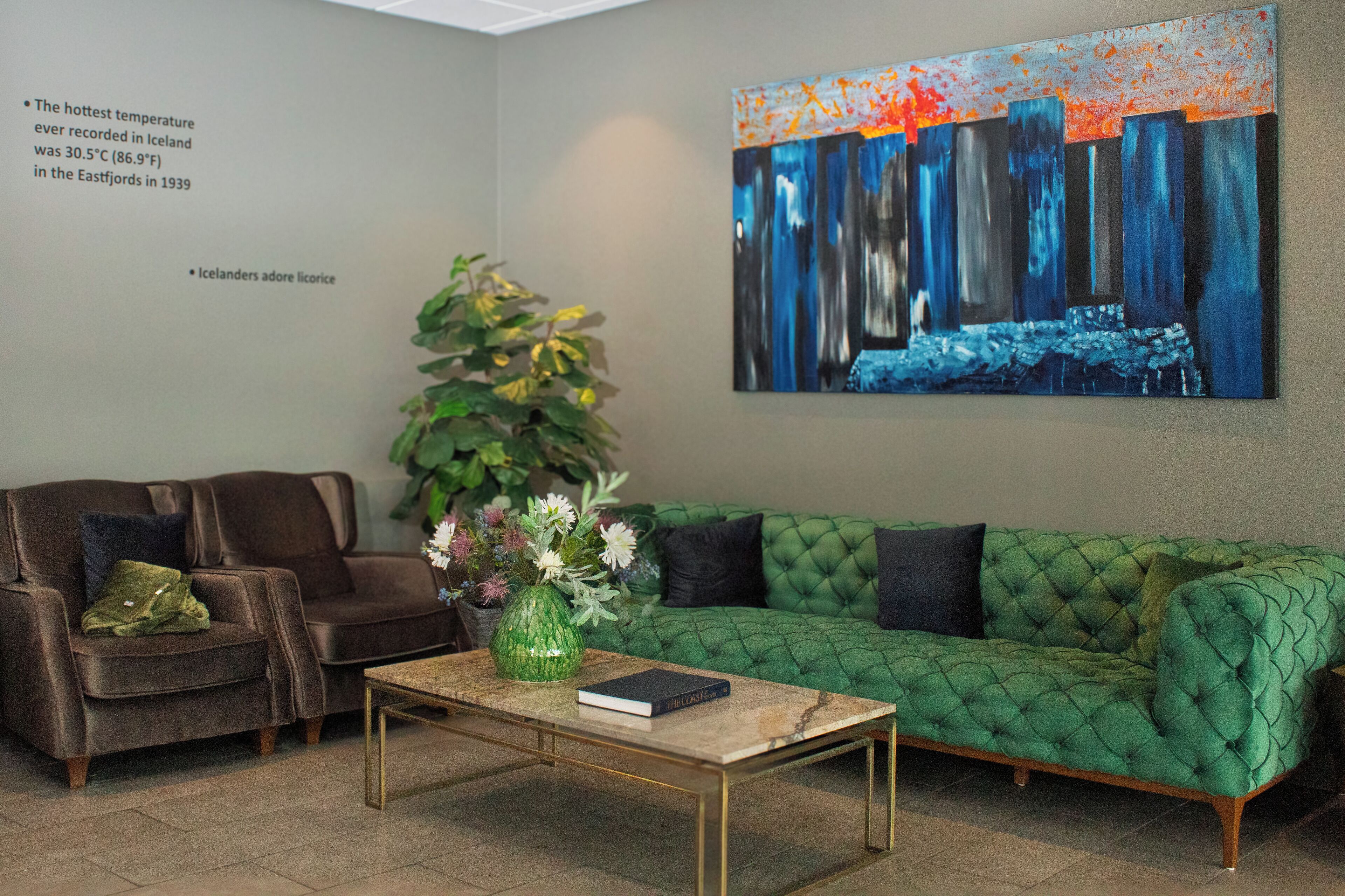 A modern living room with a brown leather sofa, a green tufted sofa, a marble coffee table, and a large abstract painting on the wall.