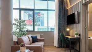 A modern living room with a leather sofa, a coffee table with books, a TV mounted on the wall, and a dining area with a table and chairs. - Hótel Múli (Reykjavik)