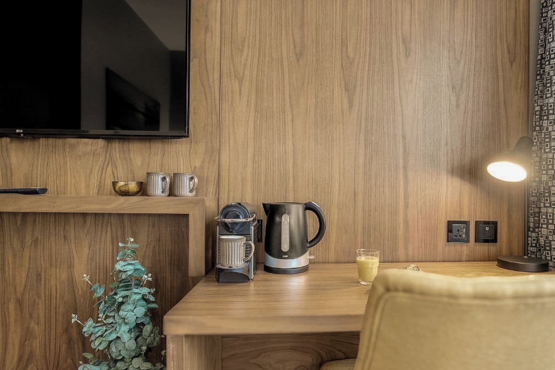 Una cocina moderna con paneles de madera, una cafetera, un hervidor y un vaso de leche sobre una mesa de madera.