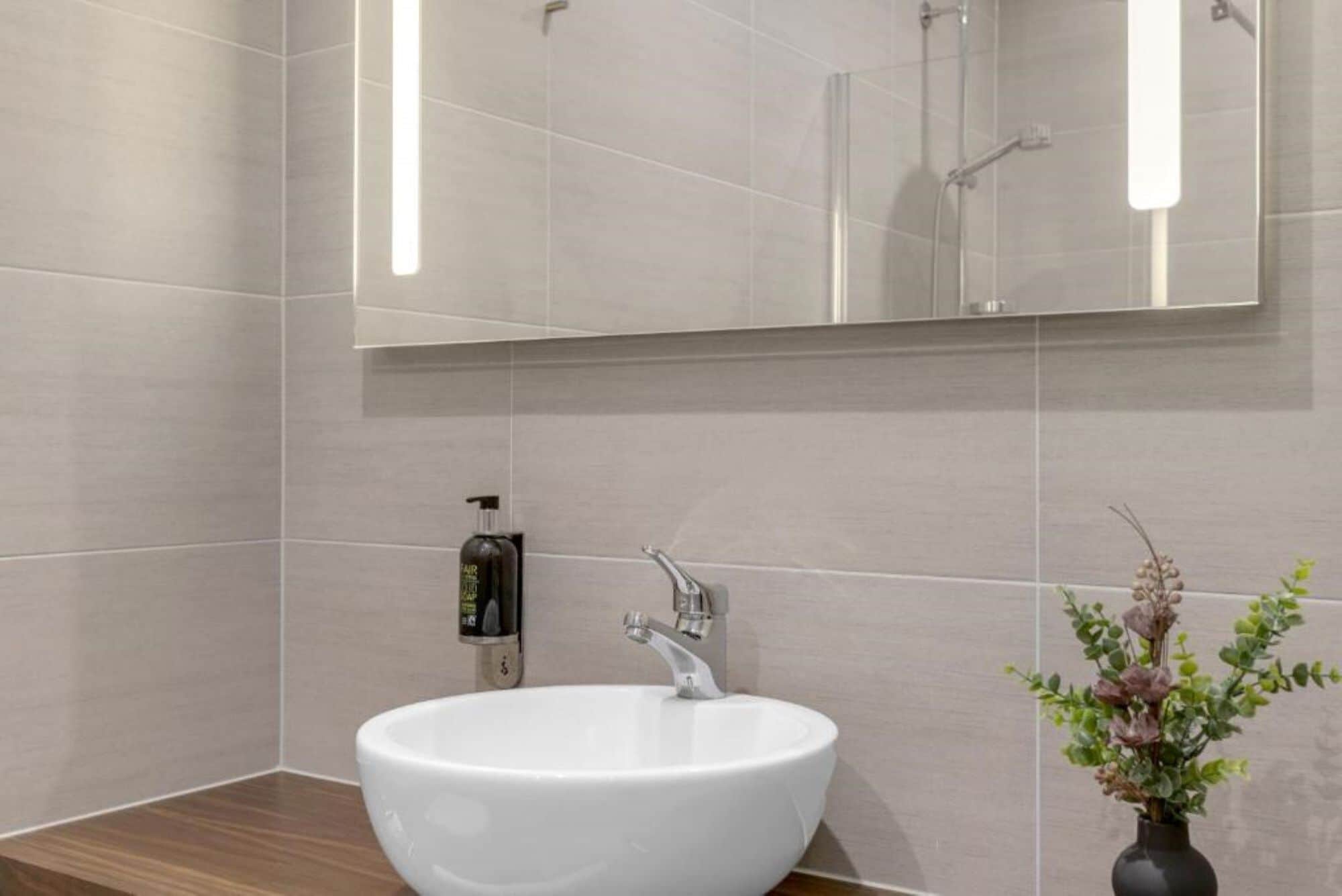 Un baño moderno con lavamanos blanco, espejo y una pequeña planta en maceta.