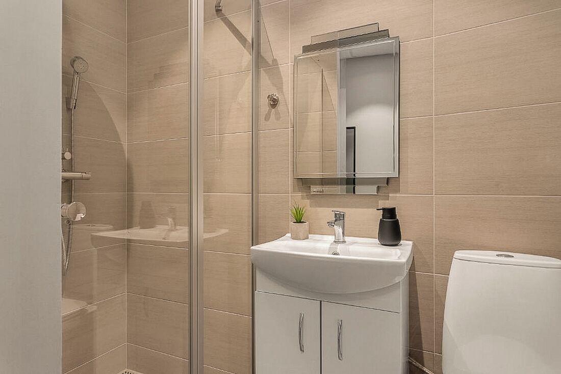 Une salle de bain moderne avec une douche à parois de verre, un lavabo blanc avec un miroir au-dessus et des toilettes.