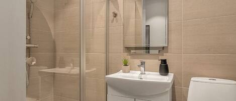 Une salle de bain moderne avec une douche à parois de verre, un lavabo blanc avec un miroir au-dessus et des toilettes.