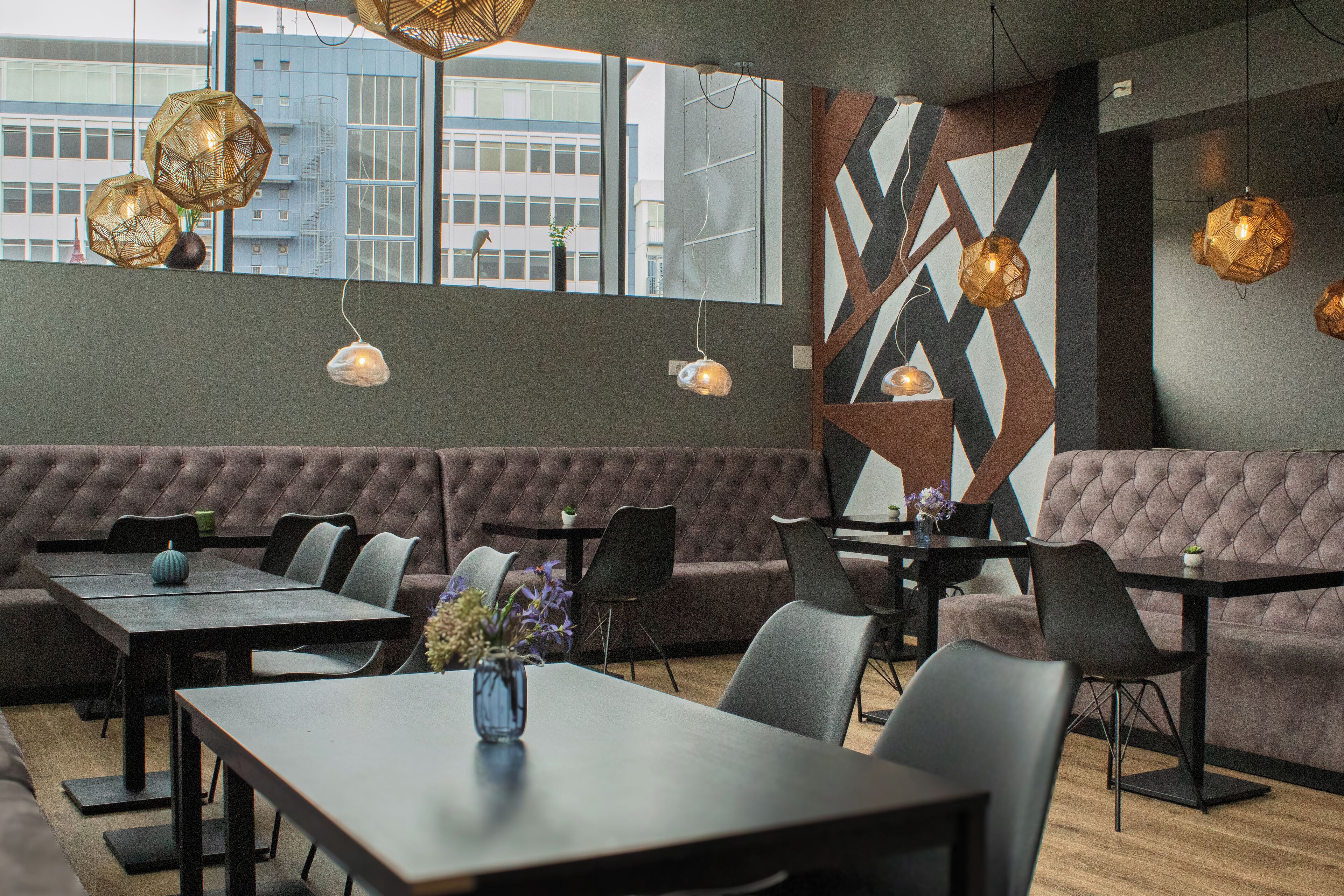 Een modern restaurant met diverse zitmogelijkheden, waaronder tafels en een groot, bekleed bankgedeelte.