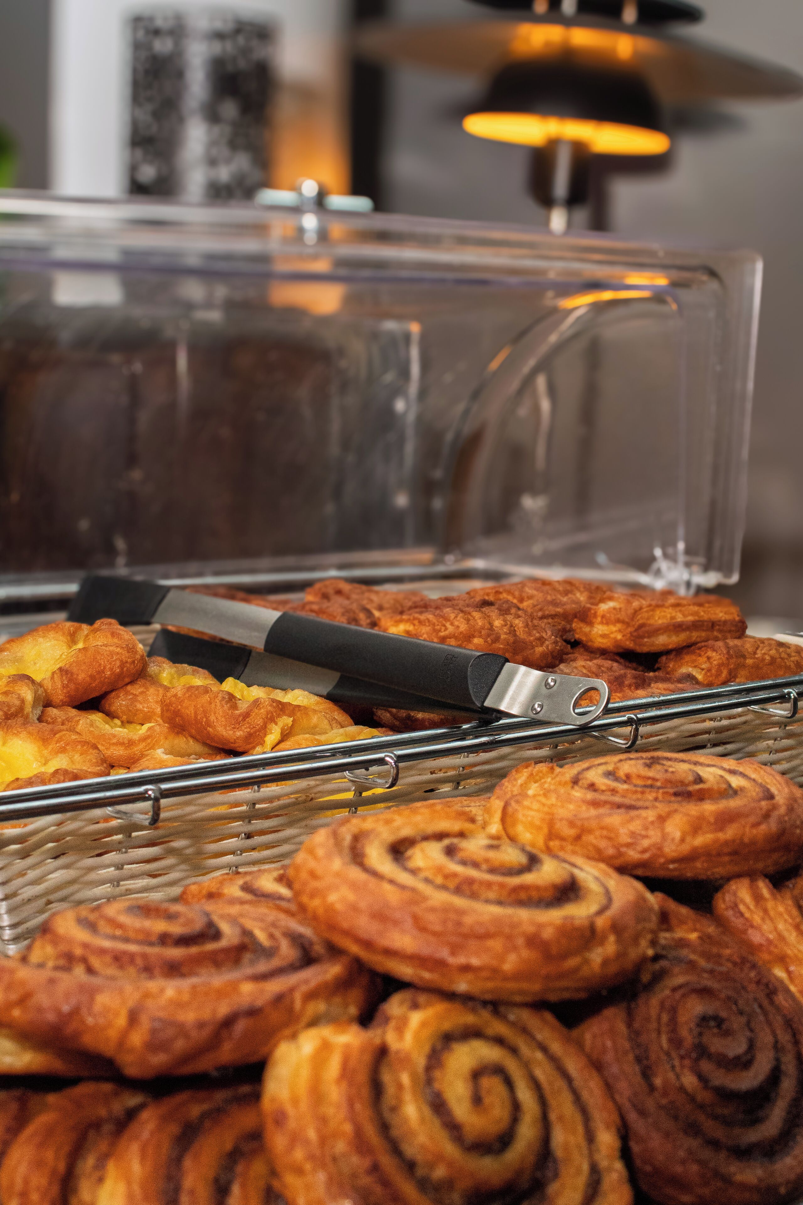 Un bufé con pastelería, incluyendo cruasanes y rollos de canela, y un recipiente transparente con un utensilio encima.