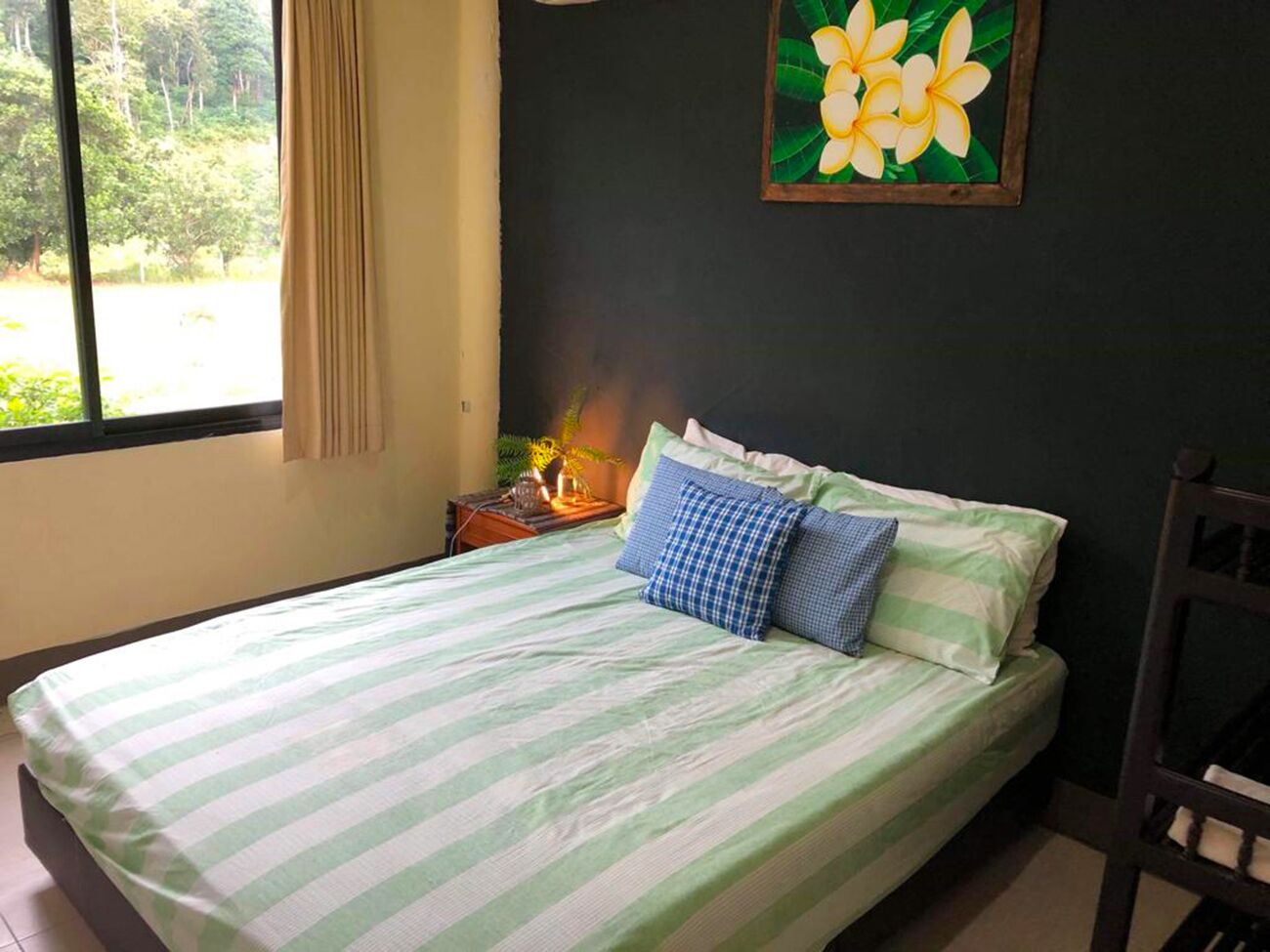 A bed with striped bedding, a nightstand with a lamp, and a painting of flowers on the wall.