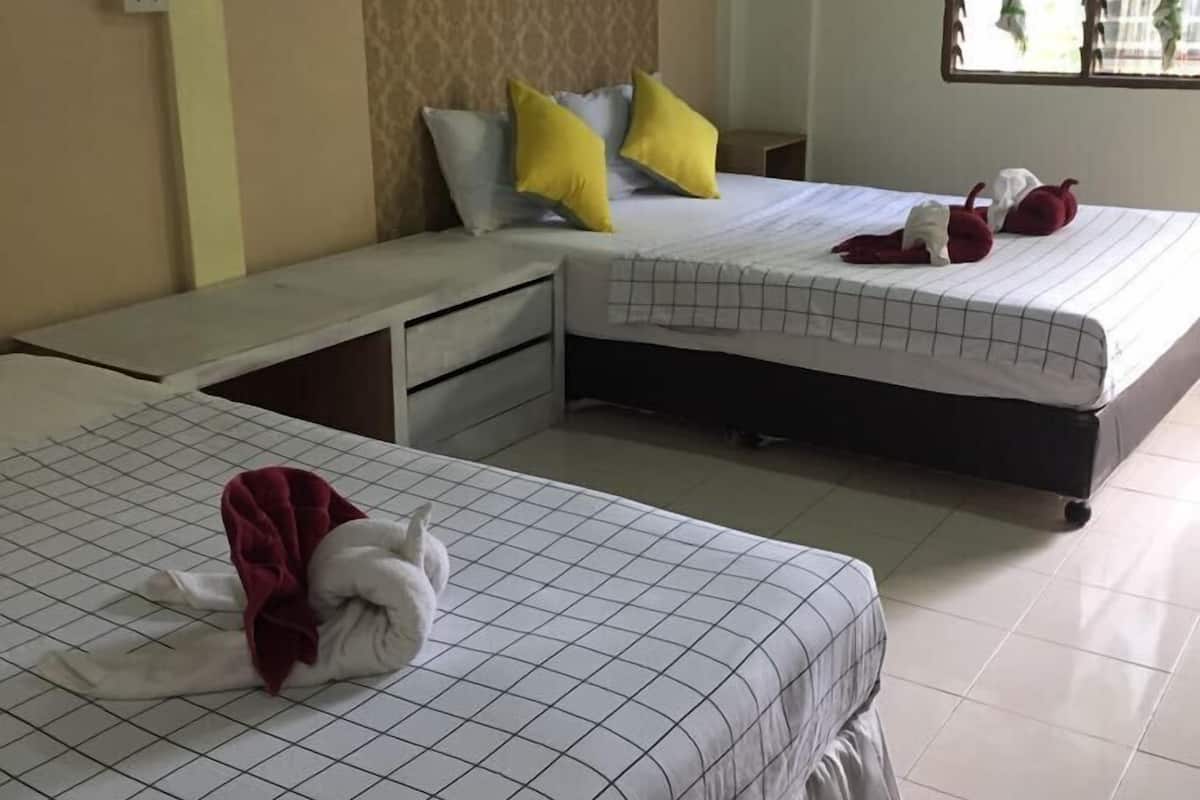 Habitación de hotel con dos camas, cada una con cubrecama y almohadas de estampado de cuadrícula. Hay un banco entre las camas, una mesita y un equipo de aire acondicionado en la pared.
