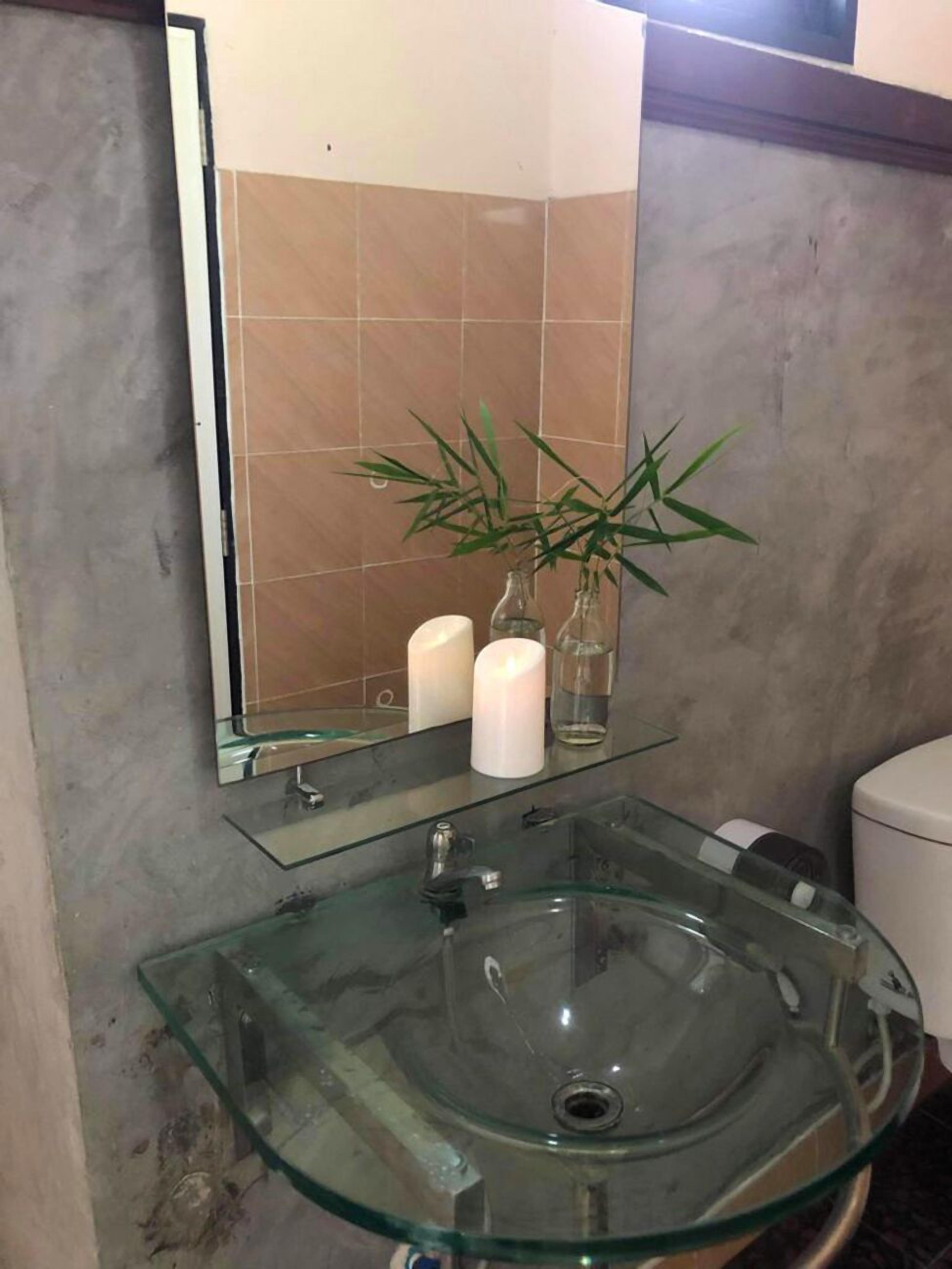 A bathroom with a glass sink, two white candles, and a bamboo plant.