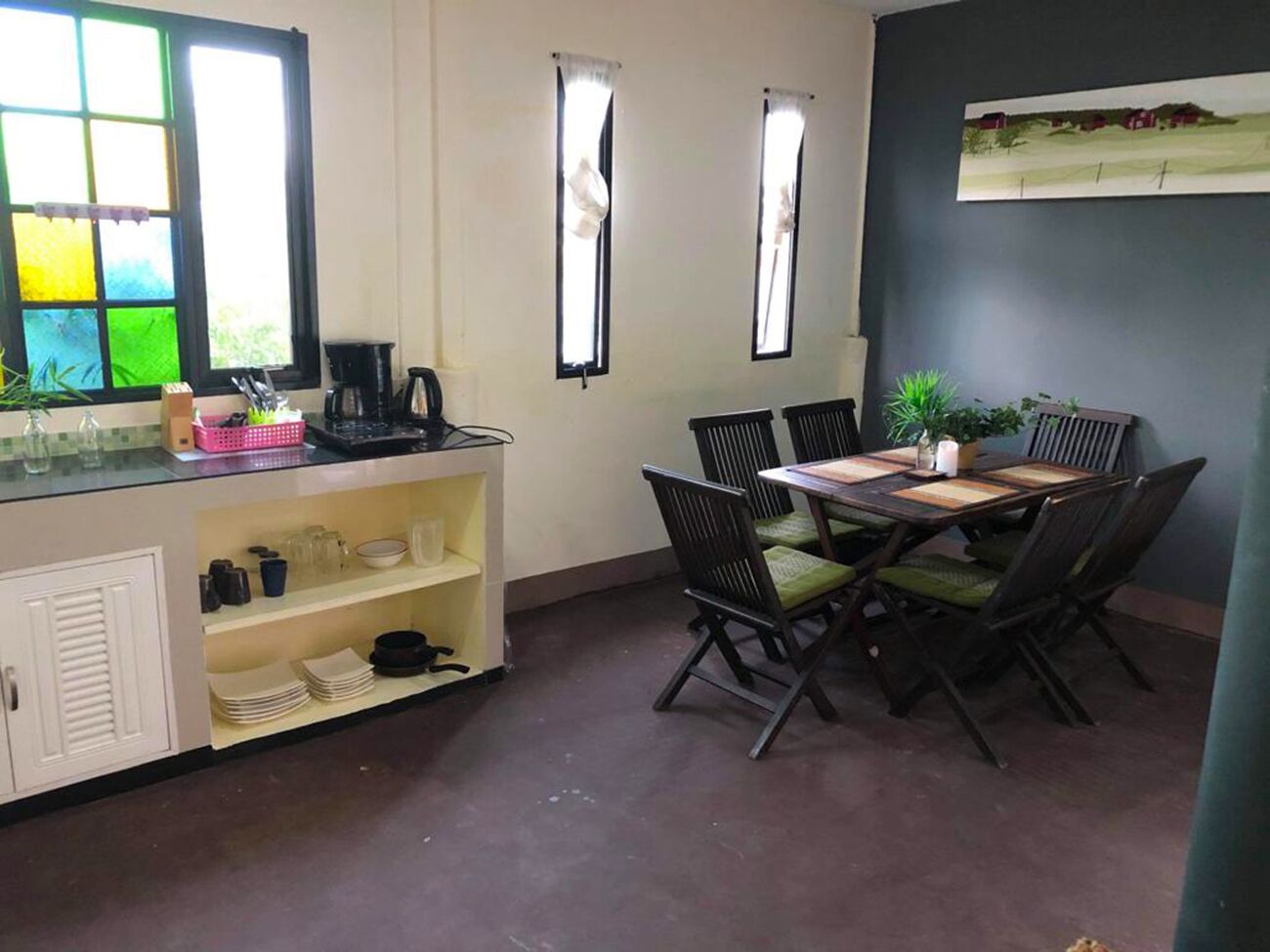 A dining area with a table and chairs, a kitchen counter with various items, and windows with curtains.