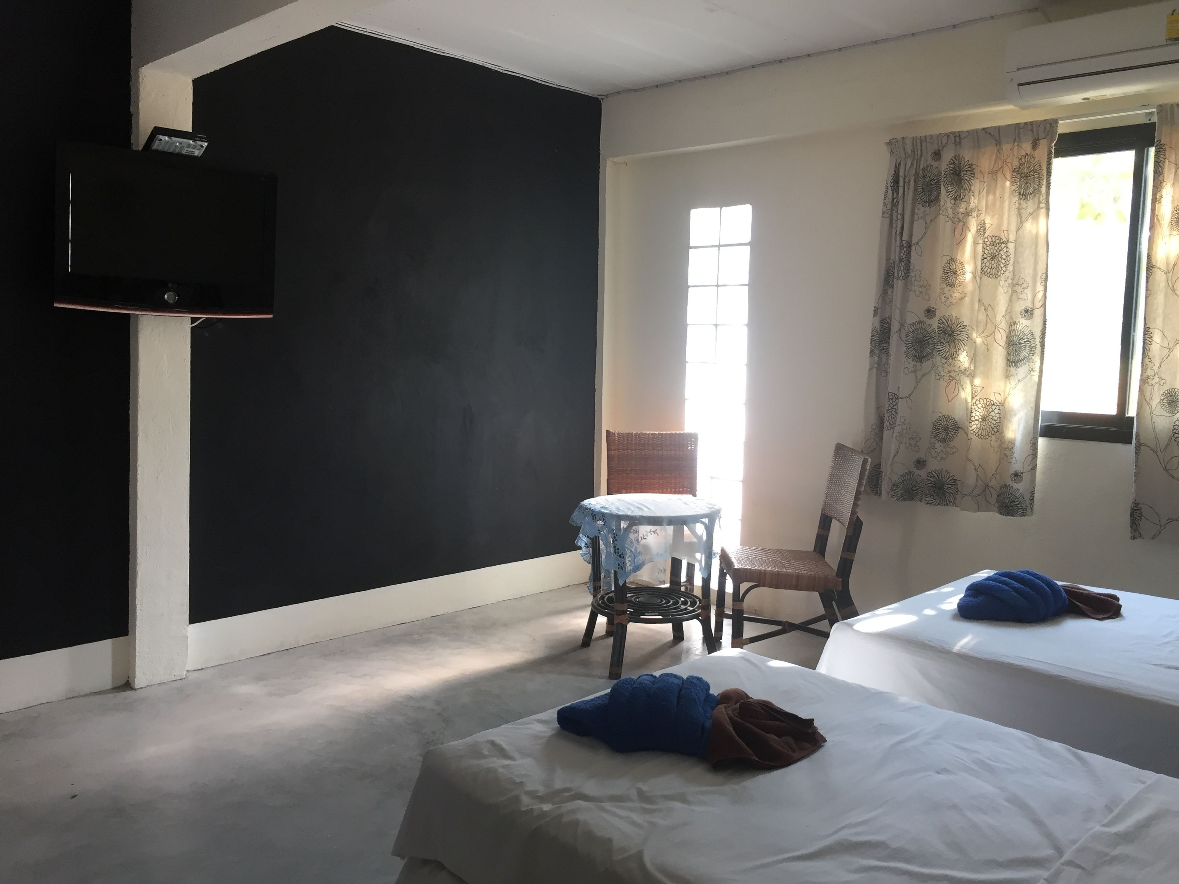 Habitación con dos camas, una mesa y una silla. Se ve un ventanal con cortinas y un televisor montado en la pared.