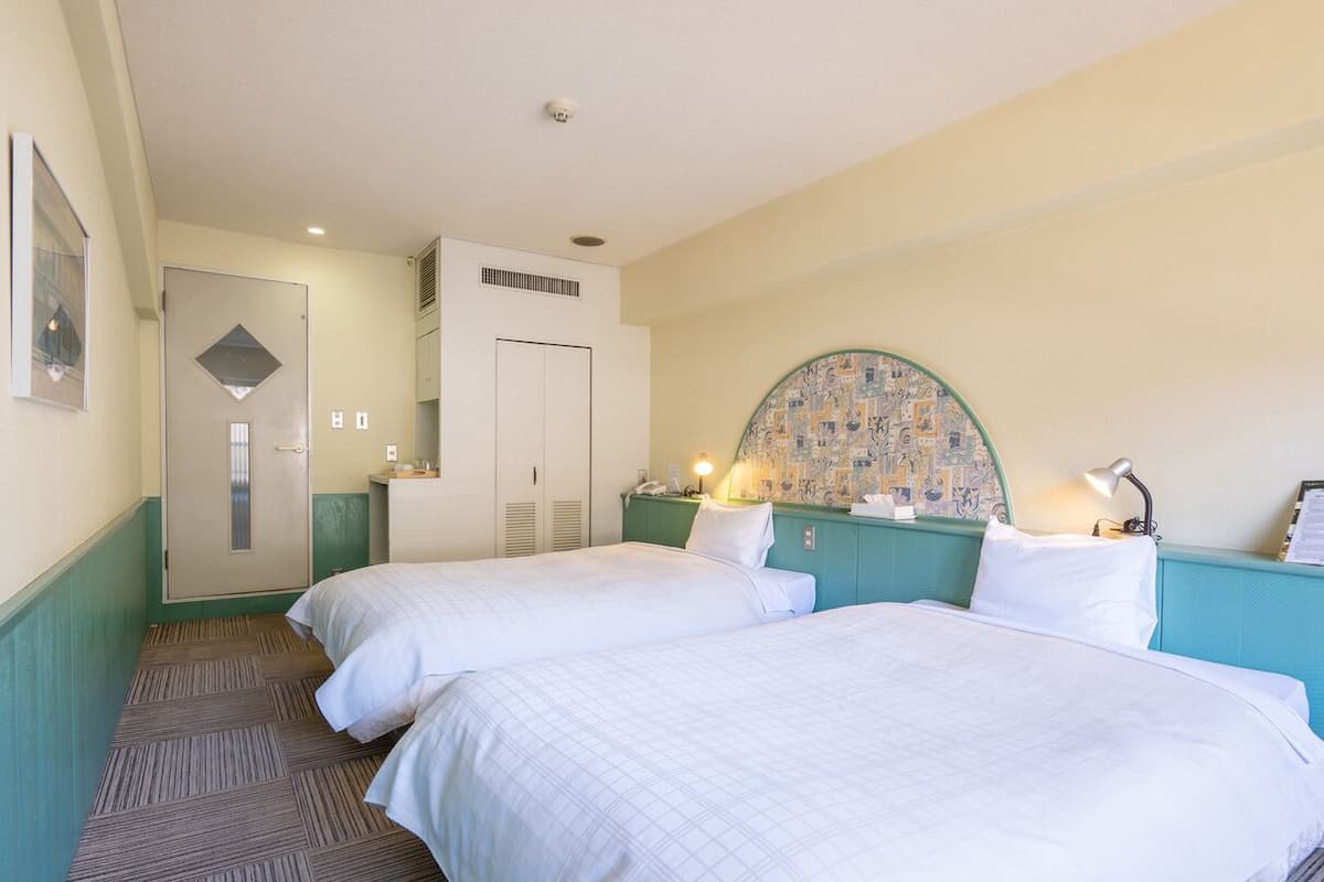 Een hotelkamer met twee bedden, een garderobe, een bureau met een lamp en een decoratieve wand.