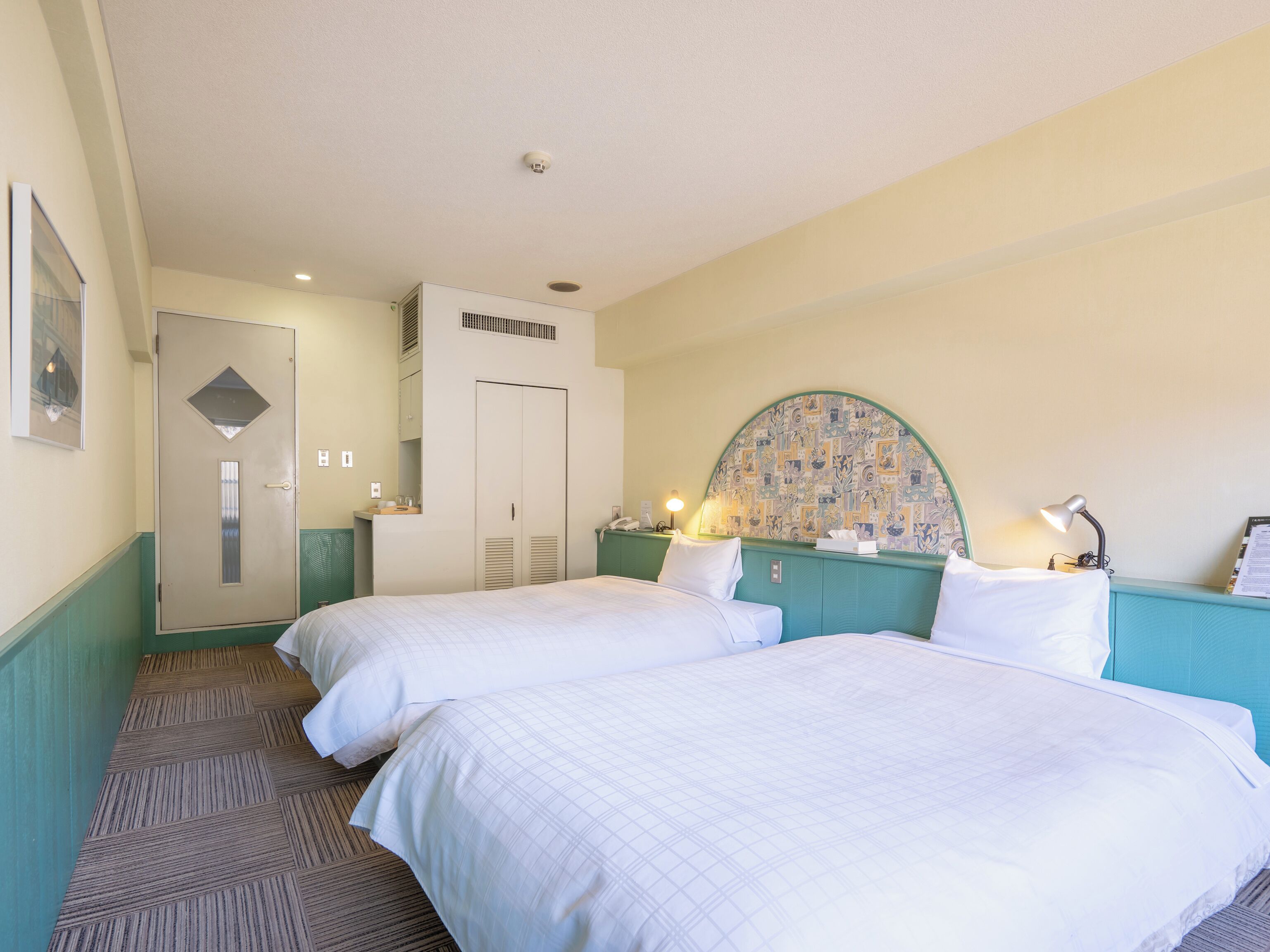 Una habitación de hotel con dos camas, un baño y un pequeño escritorio con lámpara.