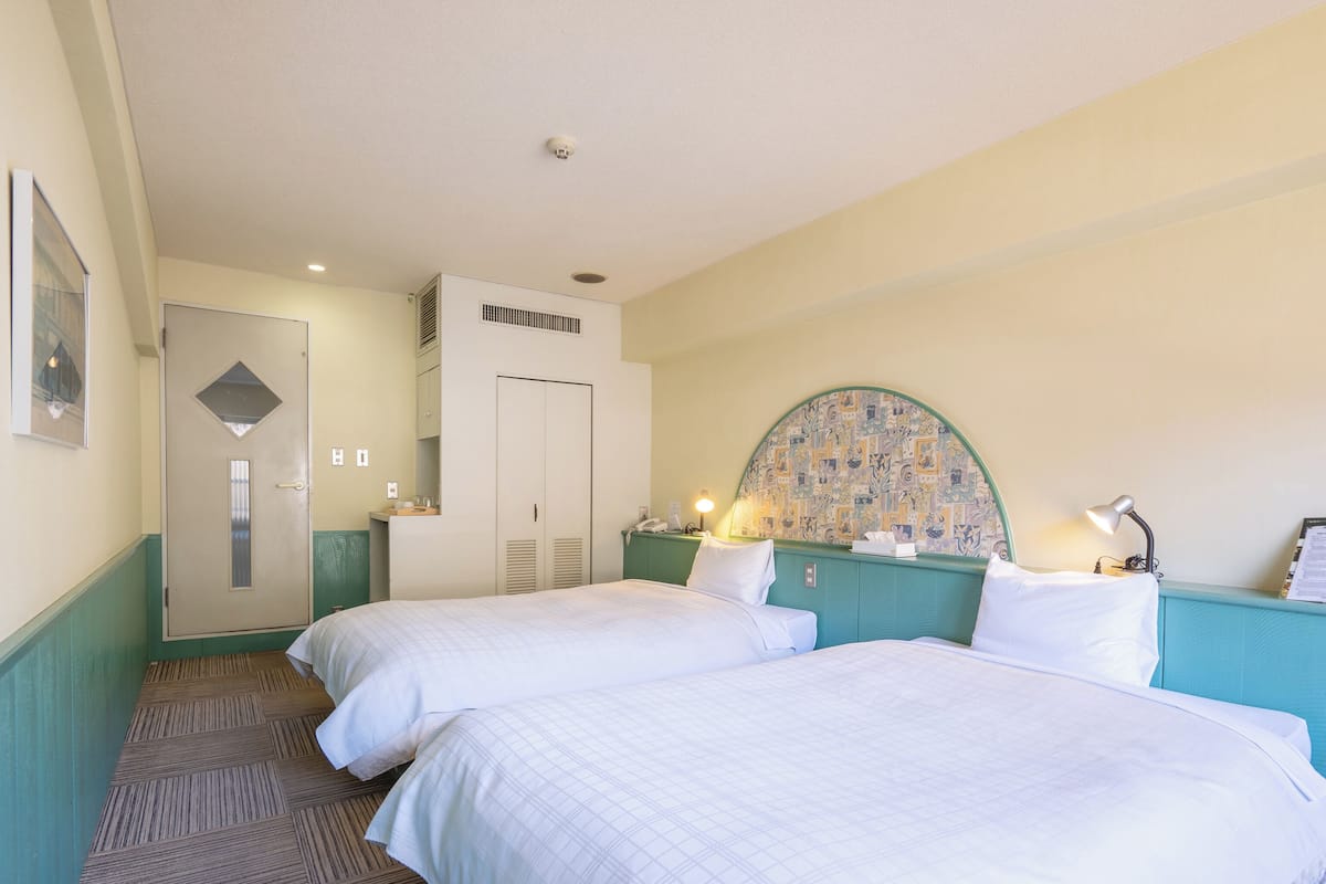 Een hotelkamer met twee bedden, een badkamer en een klein bureau met een lamp.