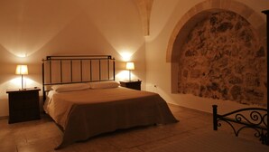 A bedroom with a bed, two bedside tables, a lamp, and a stone wall.