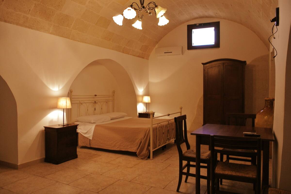 A bedroom with a bed, bedside tables, a desk, and a chair. There is a window with a view of the outside.