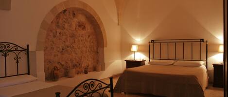 A bedroom with a stone fireplace, a bed, a bedside table with a lamp, and a nightstand.