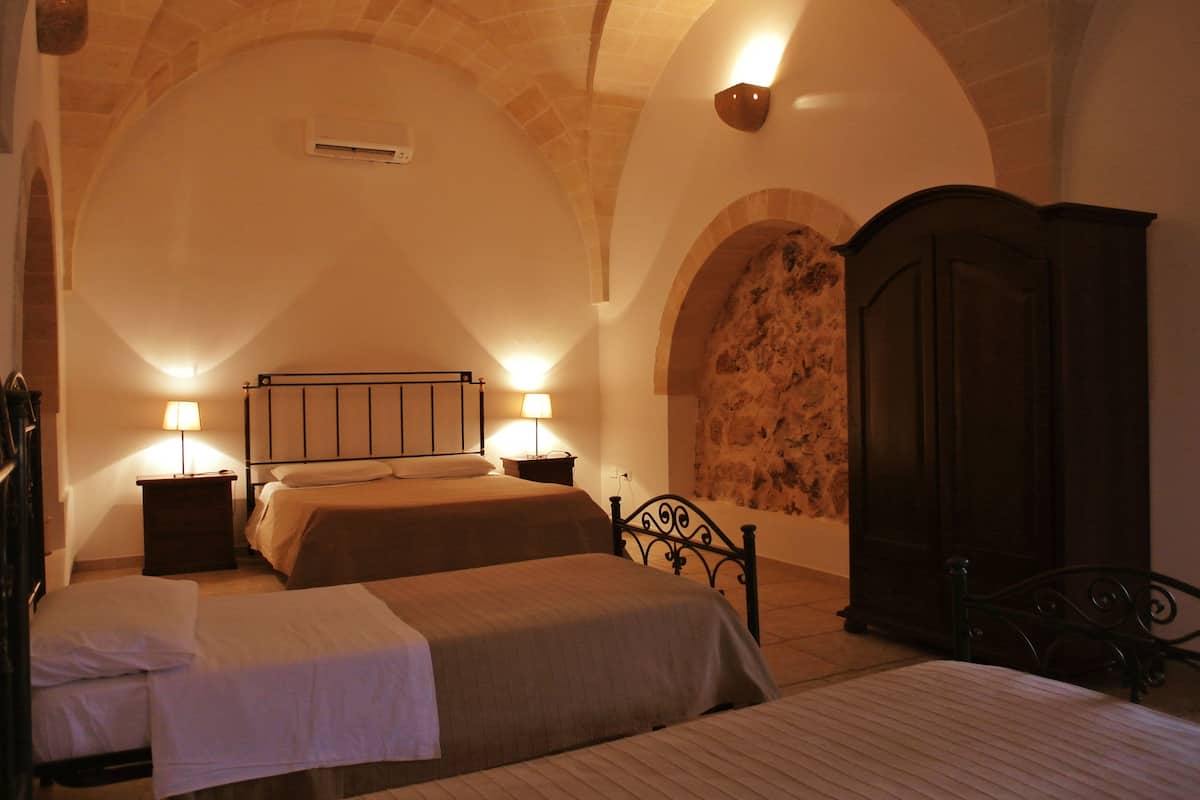 A bedroom with two beds, a stone wall, and a dark wooden wardrobe.