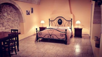 Een slaapkamer met een bed, twee nachtkastjes met lampen, een stoel en een stenen muur.