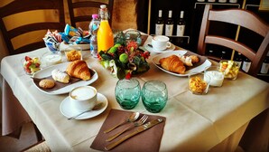 A breakfast table with croissants, fruit, coffee, and wine bottles.