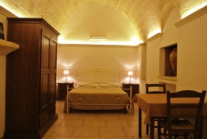 A bedroom with a bed, bedside tables with lamps, a wooden wardrobe, and a dining table with chairs. - Agriturismo Masseria Nuova (Francavilla Fontana)