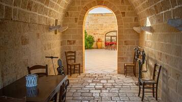 Una stanza in pietra ad arco con un tavolo e sedie, una finestra e vista su un’area esterna con tavolo e sedie.