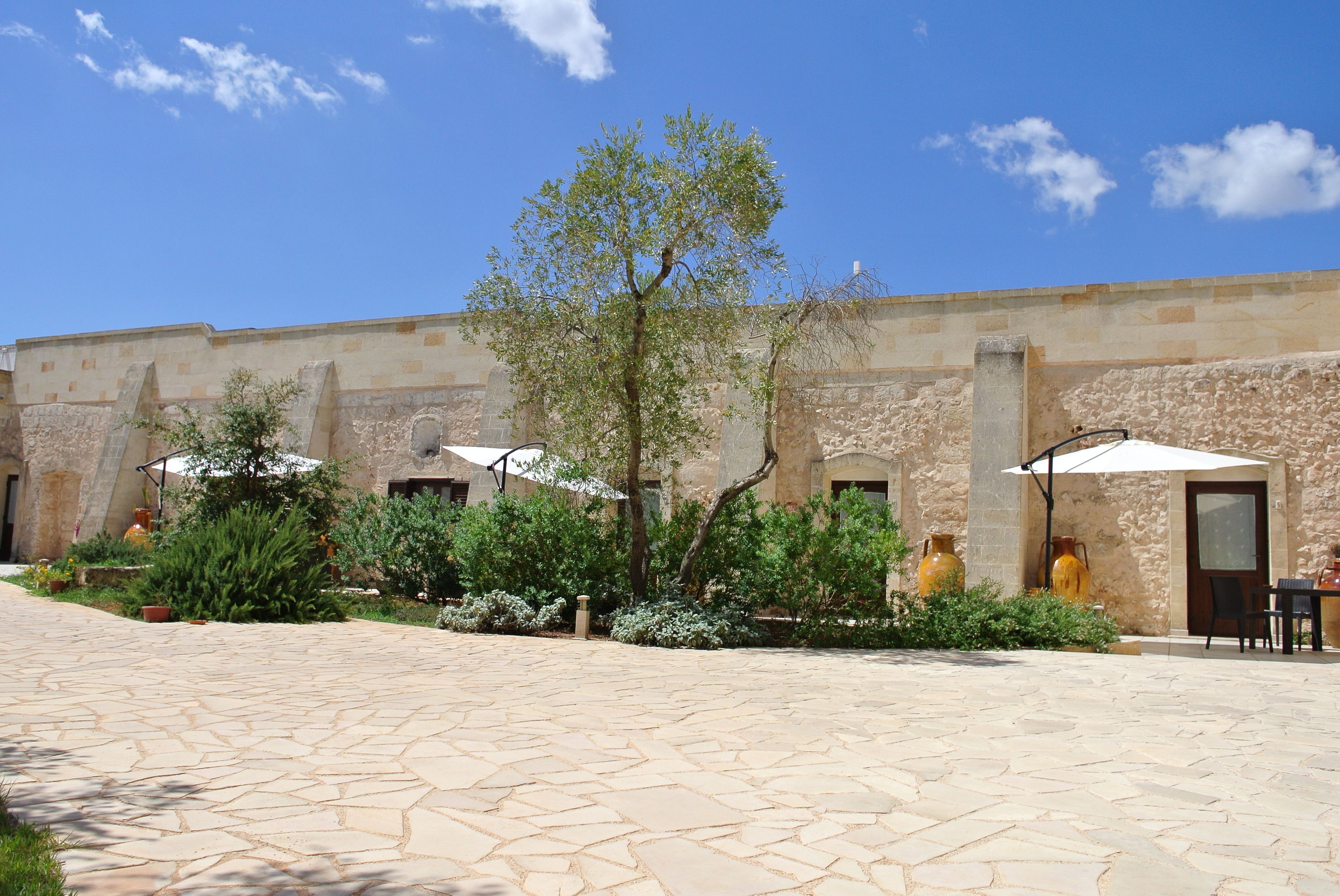 A courtyard with stone flooring, outdoor seating, and a building with stone walls and a tiled roof.