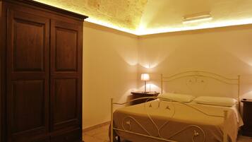 Een slaapkamer met een bed, een houten garderobe en een nachtkastje met een lamp.