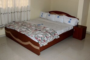 A bed with a floral bedspread, white pillows with a logo, and a wooden headboard. - Grace Inn Hotel (Kwabenya)