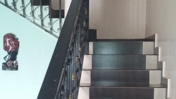 Una escala amb trams alternats de colors fosques i clares, una barana de metall negre amb detalls decoratius i una columna blanca a la dreta.