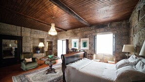 A rustic bedroom with a stone wall, wooden ceiling, and a large bed with white linens. - Casa do Ribeiro (Guimarães)