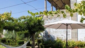 A patio with a table and chairs, a hammock, and a pergola with a white umbrella. - Casa do Ribeiro (Guimarães)