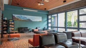 A modern lounge area with seating, a bookshelf, and a large window offering a view of the outdoors. - Youth Hostel Zurich (Zürich)