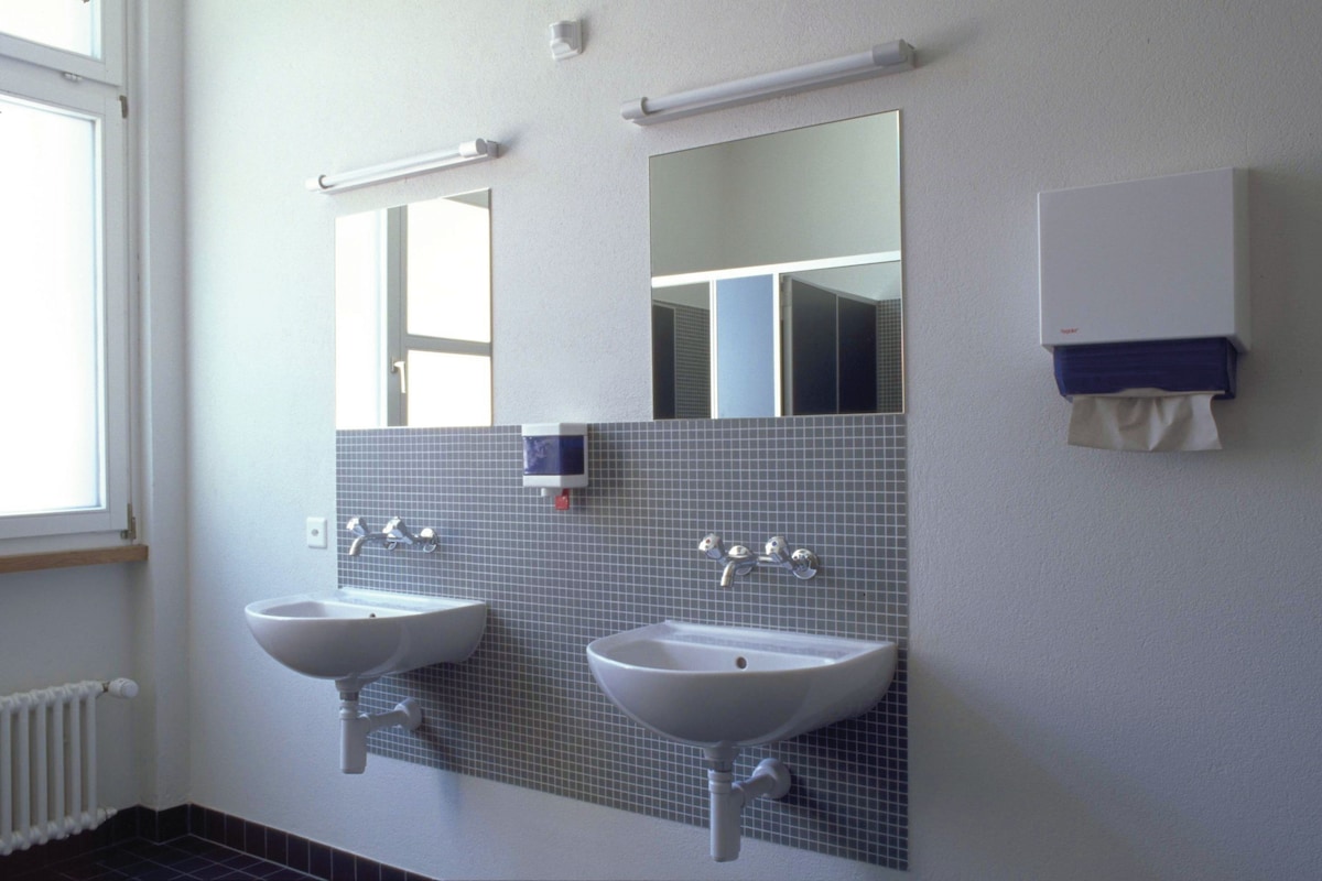 A bathroom with two sinks, a mirror, and a towel dispenser.