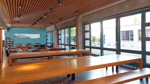 A modern library with wooden benches, large windows, and a mural on the wall. - Youth Hostel Zurich (Zürich)
