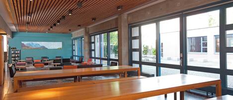 A modern library with wooden benches, large windows, and a mural on the wall.