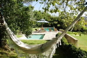 Un hamac dans un jardin luxuriant, avec une piscine et du mobilier d’extérieur.